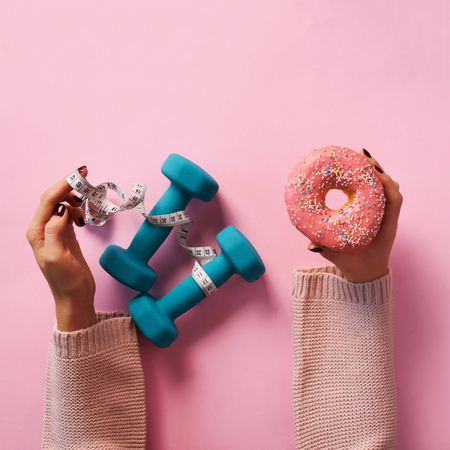 Female hand holding sweet donut, measuring tape, dumbbells over pinkの写真素材