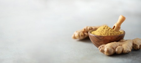 Ginger root and ginger powder in wooden bowl over grey concrete  with copy space.の写真素材