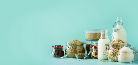Glass bottles of vegan plant milk and almonds, nuts, coconut, hemp seed milk on blue