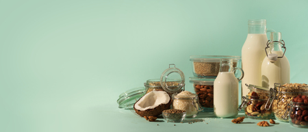 Vegan substitute dairy milk. Glass bottles with non-dairy milk and ingredients over blueの写真素材