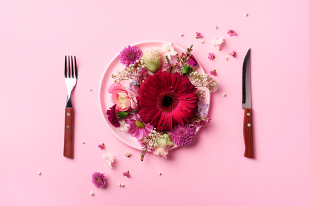 Pink flowers on pink plate, fork, knife over punchy pastelの写真素材