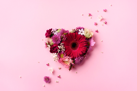 Heart shape made of spring flowers on pink punchy pastelの写真素材