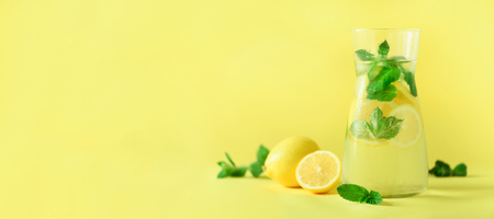 Detox water with mint, lemon on yellow background. Banner with copy space. Citrus lemonade. Summer fruit infused waterの写真素材