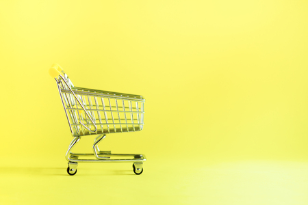 Shopping cart on yellow background. Minimalism style. Creative design. Copy space. Shop trolley at supermarket. Sale, discount, shopaholism concept. Consumer society trend.の写真素材