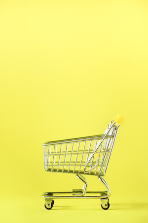 Shopping cart on yellow background. Minimalism style. Creative design. Copy space. Shop trolley at supermarket. Sale, discount, shopaholism concept. Consumer society trend.の写真素材