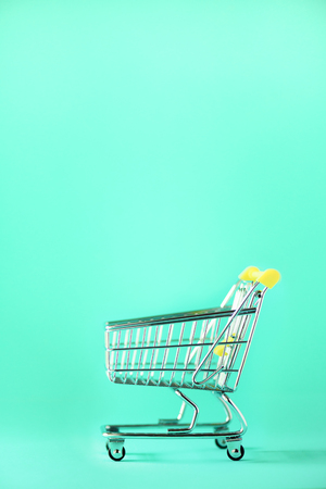 Shopping cart on blue background. Minimalism style. Creative design. Copy space. Shop trolley at supermarket. Sale, discount, shopaholism concept. Consumer society trend.の写真素材