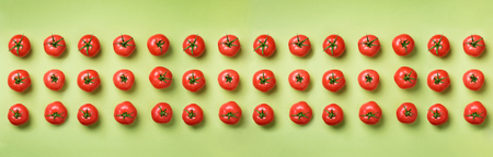 Creative pattern of red tomatos on green background. Top view. Copy space. Minimal design. Vegetarian, vegan, organic food and alkaline meal concept.の写真素材