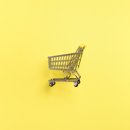 Shopping cart on yellow background. Minimalism style. Creative design. Top view with copy space. Shop trolley at supermarket. Sale, discount, shopaholism concept. Consumer society trend.の写真素材