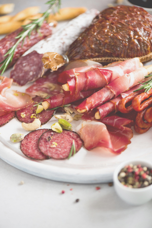 Cold smoked meat plate. Traditional italian antipasto, cutting board with salami, prosciutto, ham, pork chops, olives on greyの写真素材
