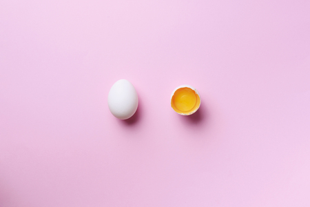 Food concept with broken egg and whole one on pink background. Top view. Creative pattern in minimal style. Flat lay.の写真素材