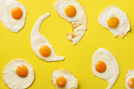 Fried eggs or scrambled eggs pattern on yellow background. Creative food concept. Top view. Minimalistic style.の写真素材