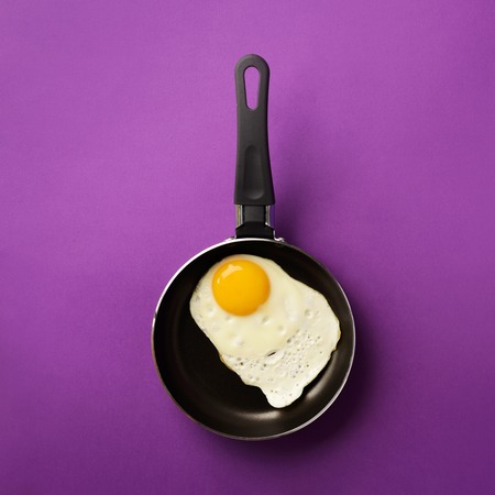 Creative food concept with fried egg on pan over violet background. Top view. Creative pattern in minimal style. Flat lay. Square crop.の写真素材