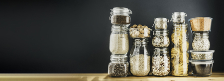 Banner with assortment of grain products and pasta in glass storage containers on wooden table.の写真素材