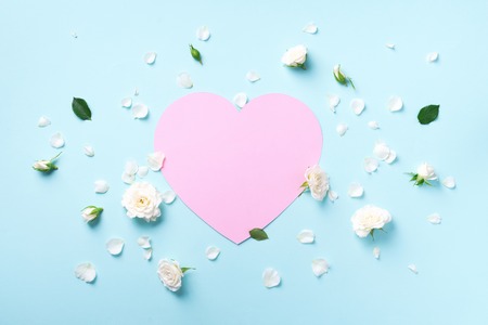 Pink paper heart, white roses and petals on blue pastel background. Spring or summer concept....