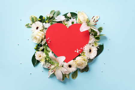 Creative layout with white roses, lily, gerbera, red paper heart over blue background. Top view, flat lay. Spring, summer or garden concept. Flowers for Woman day. Banner.の写真素材