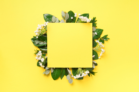 Summer and spring concept. Tropical nature background with green leaves, white flowers and white empty square frame for copy space on yellow paper. Top view. Flat lay. Creative advertising.の写真素材