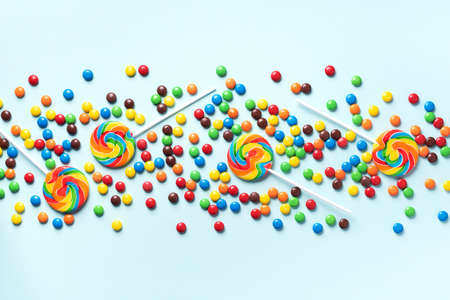 Multicolored lollipop, rainbow colorful candies on blue background. Coated chocolate sweet pieces texture. Top view. Flat lay. Confetti for holidays, birthday party concept.の写真素材