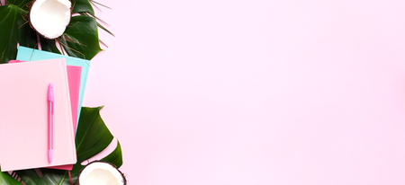 Female blog writer workspace concept. Green monstera palm leaves, coconut on pink background with copy space. Banner. Flat lay, top viewの写真素材