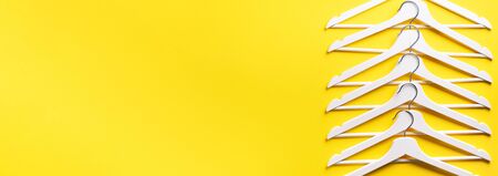 Top view of white clothes hangers on yellow background with copy space. Flat lay. Minimalism style. Creative layout. Fashion, store sale, shopping concept. Banner for feminine blog.の写真素材
