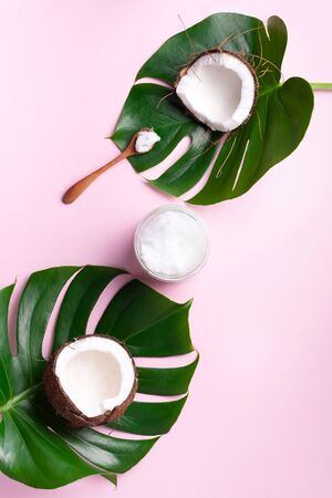 Coconut oil and ripe coconuts, tropical palm and monstera leaves on pink background with copy space. Top view. Summer creative layoutの写真素材