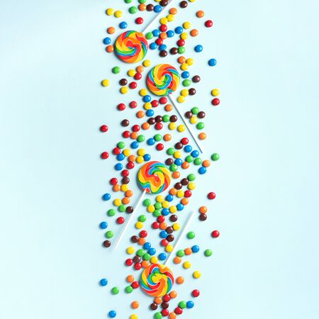 Multicolored lollipop, rainbow colorful candies on blue background. Coated chocolate sweet pieces texture. Top view. Flat lay. Confetti for holidays, birthday party concept.の写真素材
