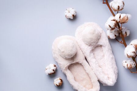 Nude fluffy home slippers with pompon, tropical palm and monstera leaon pastel grey background. Top view. Copy space. Cozy home footwear. Sweet home and spa, body treatment concept.の写真素材