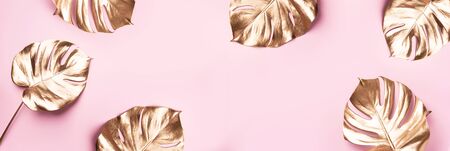 Exotic summer trend in minimal style. Golden tropical palm monstera leaf on pastel pink color background. Shiny and sparkle design, fashion conceptの写真素材