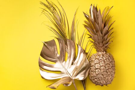 Creative layout. Gold pineapple and golden palm, monstera on yellow background with copy space. Top view. Tropical flat lay. Exotic food concept, crazy trend. Banner.の写真素材