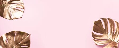 Exotic summer trend in minimal style. Golden tropical palm monstera leaf on pastel pink color background. Shiny and sparkle design, fashion conceptの写真素材
