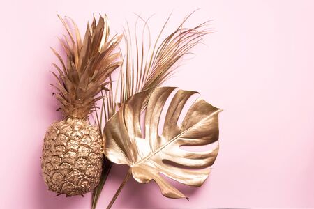 Creative layout. Gold pineapple and golden palm, monstera on pink background with copy space. Top view. Tropical flat lay. Exotic food concept, crazy trend. Banner.の写真素材