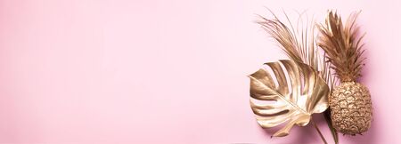 Creative layout. Gold pineapple and golden palm, monstera on pink background with copy space. Top view. Tropical flat lay. Exotic food concept, crazy trend. Banner.の写真素材