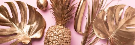 Golden exotic fruits, tropical palm, monstera leaves on pink background. Top view. Flat lay. Food concept. Creative layout of gold pineapple, banana, lemon with copy spaceの写真素材
