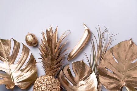 Creative layout. Gold pineapple and golden palm, monstera on grey background with copy space. Top view. Tropical flat lay. Exotic food concept, crazy trend. Banner.の写真素材