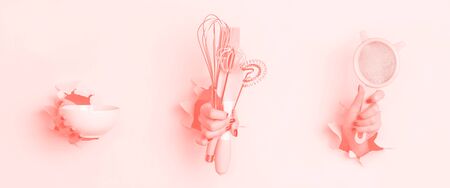 Woman hand holding kitchen utensils on trendy coral color background. Baking tools - brush, whisk, spatula. Bakery, cooking, healthy homemade food concept. Copy space.の写真素材