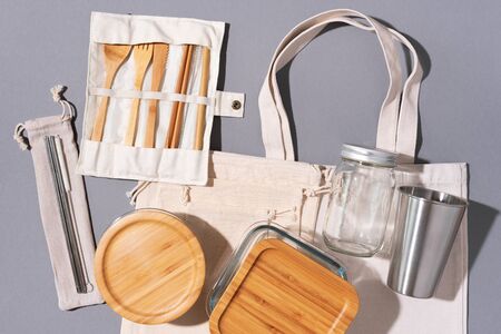 Cotton bags, glass jar, bottle, metal cup, straws for drinking, bamboo cutlery and boxes on gray...