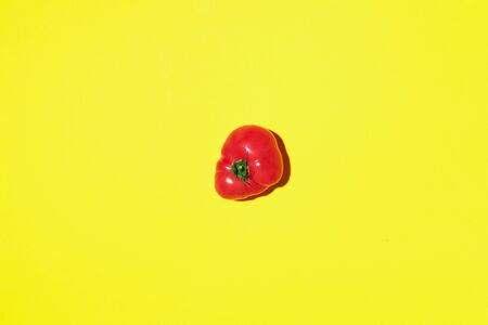 Red tomato on yellow background with copy space. Top view. Flat lay. Summer minimal concept. Vegan...