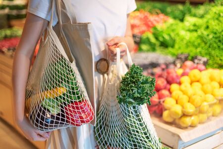 Zero waste concept with copy space. Woman holding cotton shopper and reusable mesh shopping bags with vegetables, products. Eco friendly mesh shopper. Zero waste, plastic free conceptの写真素材