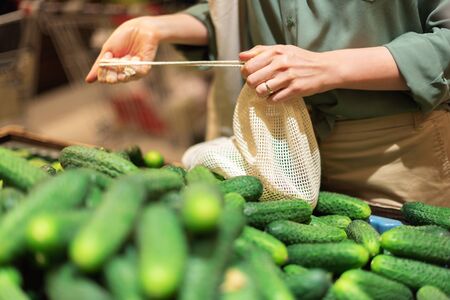 Zero waste, plastic free concept. Sustainable lifestyle. Woman chooses fruits and vegetables at farmers market. Reusable cotton and mesh eco bags for shoppingの写真素材