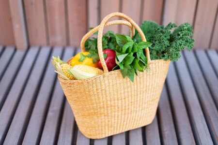 Girl holding basket with healthy organic vegetables, wooden background, copy space. Autumn harvest. Zero waste, plastic free concept. Sustainable lifestyle. Thanksgiving day.の写真素材