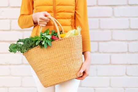 Young girl holding straw basket with vegetables, products without plastic bags, brick background. Zero waste, plastic free concept. Sustainable lifestyle. Bannerの写真素材