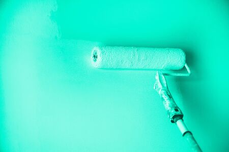 Hand painting wall with paint roller in mint color. Appartment renovation, repair, building and home concept. Trendy green and turquoise color. Copy space, banner. Tools for painting wallsの写真素材