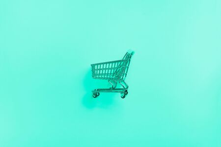 Shopping cart on mint color background. Minimalism style. Shop trolley at supermarket. Trendy green and turquoise color. Sale, discount, shopaholism concept. Consumer society trend.の写真素材