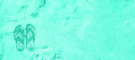Summer slippers. Flip flop on sand beach background in mint color. Copy space, top view. Trendy...