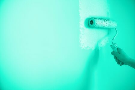 Hand painting wall with paint roller in mint color. Appartment renovation, repair, building and home concept. Trendy green and turquoise color. Copy space, banner. Tools for painting wallsの写真素材