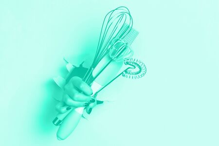 Woman hand holding kitchen utensils on mint color background. Baking tools - brush, whisk, spatula....
