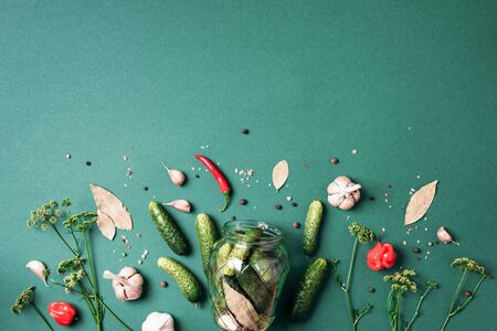 Pickling cucumbers in cans. Ingredients for marinated gherkins, glass jar, garlic, dill, salt, pepper on green background. Top view. Copy space.の写真素材