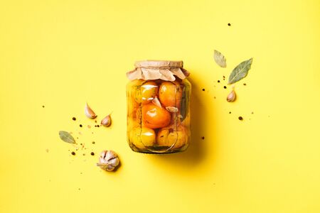 Pickled tomatoes in jar on yellow background. Top view. Flat lay. Copy space. Canned and preserved vegetables. Ingredients for vegetables preserving. Healthy fermented food conceptの写真素材