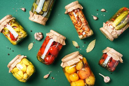 Canned and preserved vegetables in glass jars over green background. Top view. Flat lay. Copy spaceの写真素材