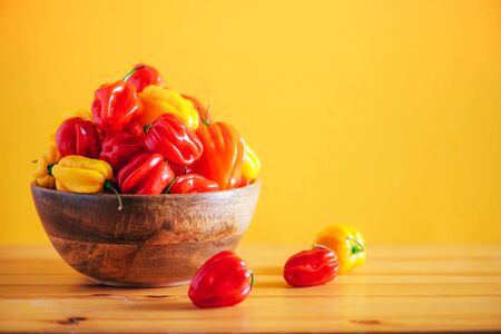 Yellow and red scotch bonnet chili peppers in wooden bowl over orange background. Copy spaceの写真素材