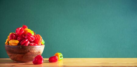 Yellow and red scotch bonnet chili peppers in wooden bowl over green background. Copy spaceの写真素材